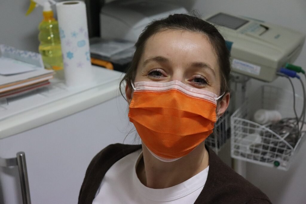 face mask, nurse, woman with mask, healthcare worker, orange mask, clinic, medical setting, safety, hospital, pandemic, protective gear, health professional, smiling eyes, female portrait, medical staff, friendly expression, covid-19, hygiene, healthcare environment, face protection, medical equipment, doctor, protective wear, indoor portrait